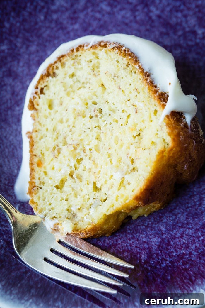 A slice of banana bundt cake with white creamy frosting on a blue plate.