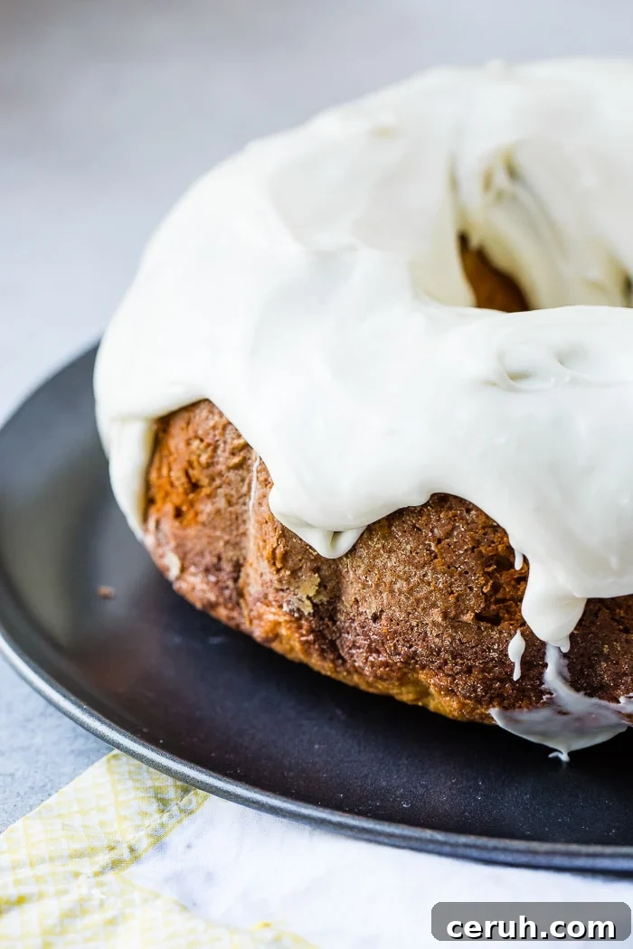 A dark grey platter with a banana pudding bundt cake slathered with cream cheese frosting