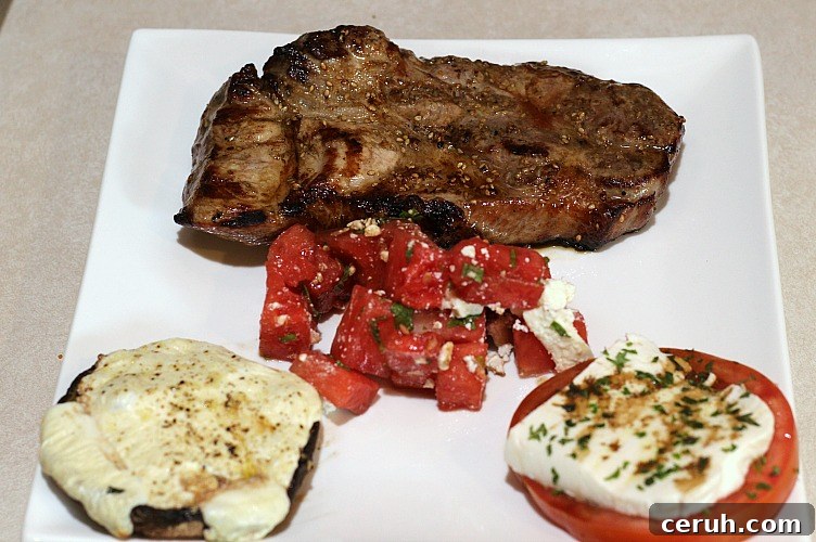 Grilled Pork steak, grilled portabella mushrooms, tomato caprese, and watermelon salad on a white plate