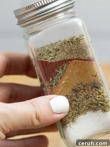 Holding a spice jar with layers of ingredients for homemade fajita seasoning Penzeys copycat recipe.