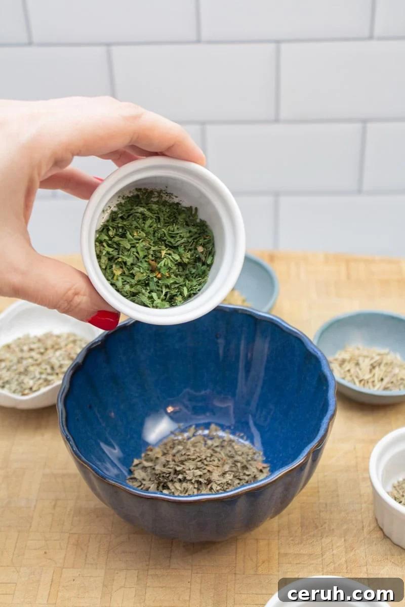 Adding dried parsley to a bowl to make an Italian spice blend.