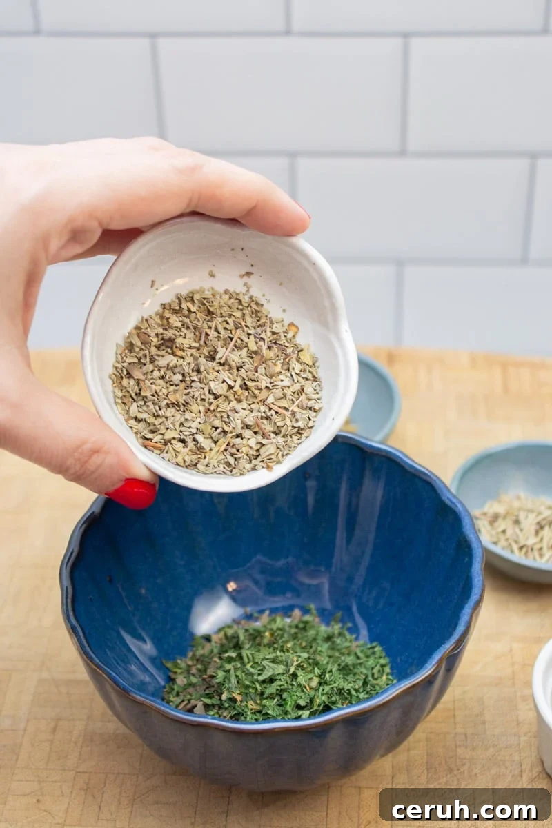 Adding dried marjoram to a bowl to make an Italian spice blend.