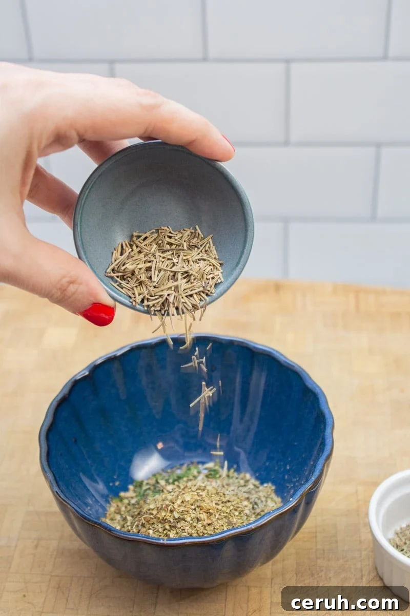 Adding dried rosemary to a bowl to make an Italian spice blend.