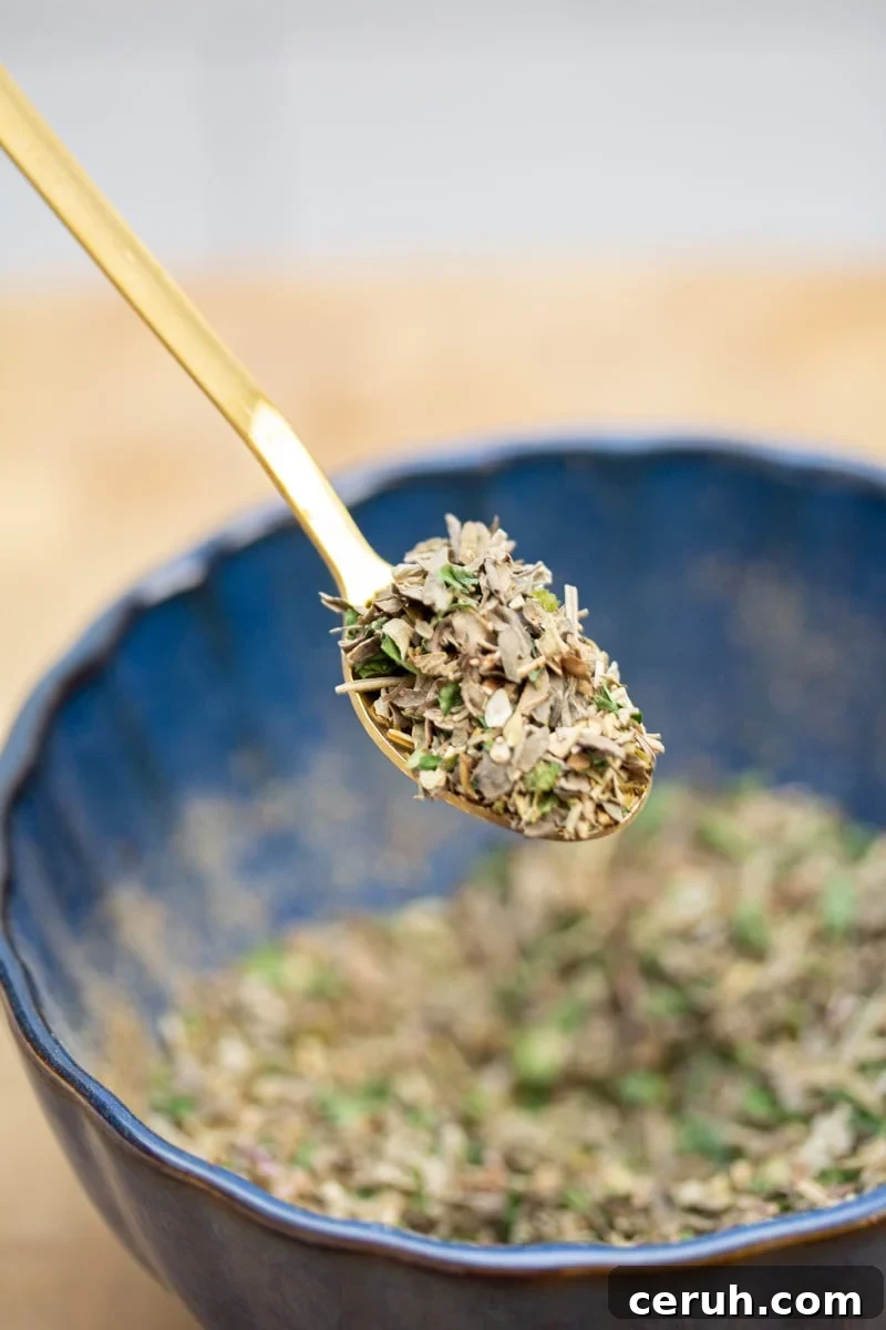 Scooping a spoonful of a homemade Italian seasoning blend from a bowl.