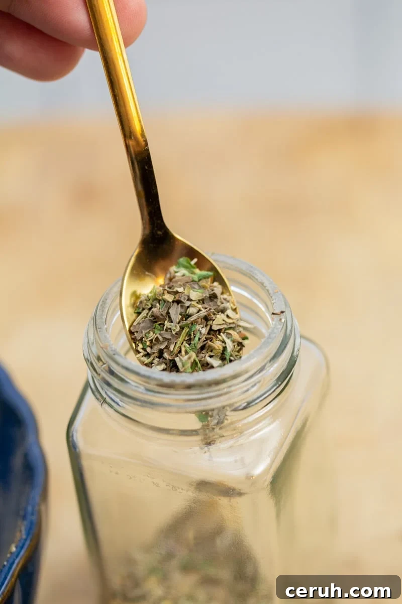 Scooping a spoonful of a homemade Italian seasoning blend into a spice jar.