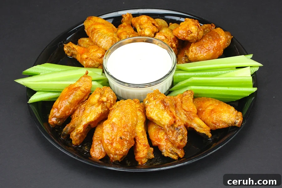 Crispy Oven Baked Chicken Wings on a round dark platter with celery sticks and blue cheese dip.