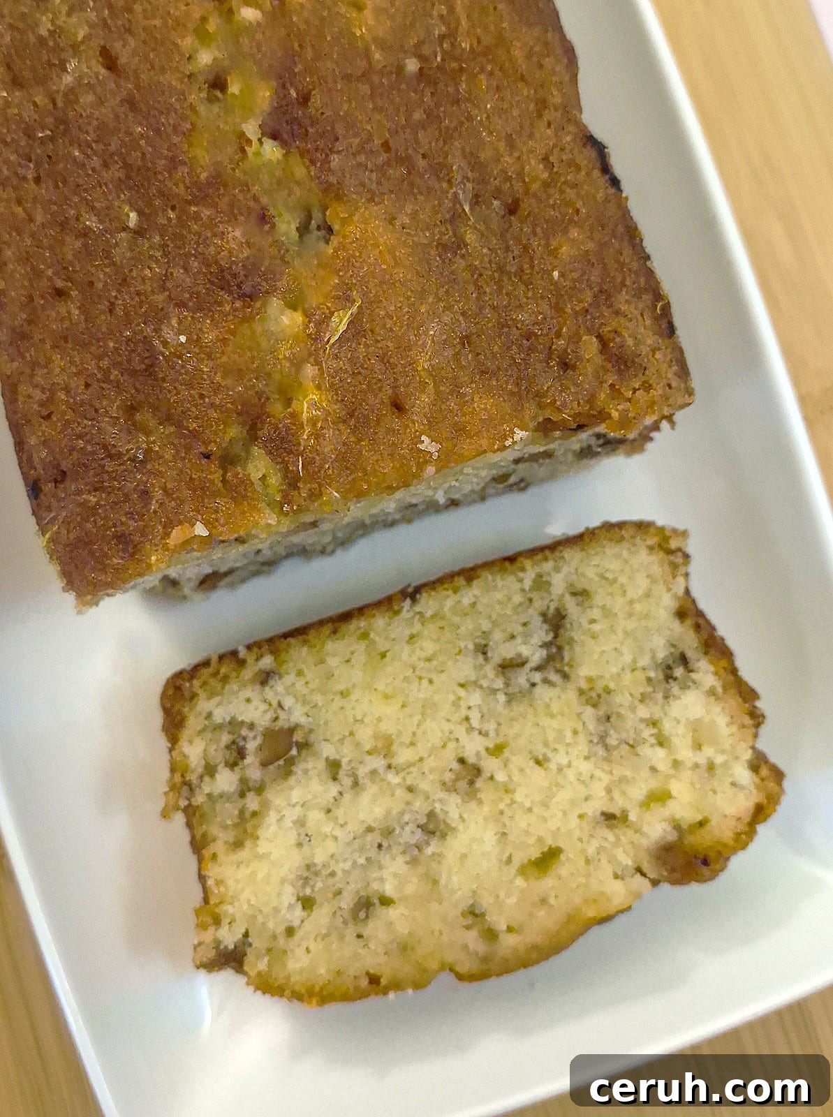 Orange Walnut Drizzle Cake with Zesty Citrus Glaze 11 Overhead shot of an orange drizzle cake, on a white platter, with a slice of cake cut from the loaf.