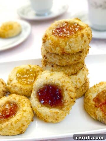 A pile of coconut jam thumbprint cookies on a white plate.
