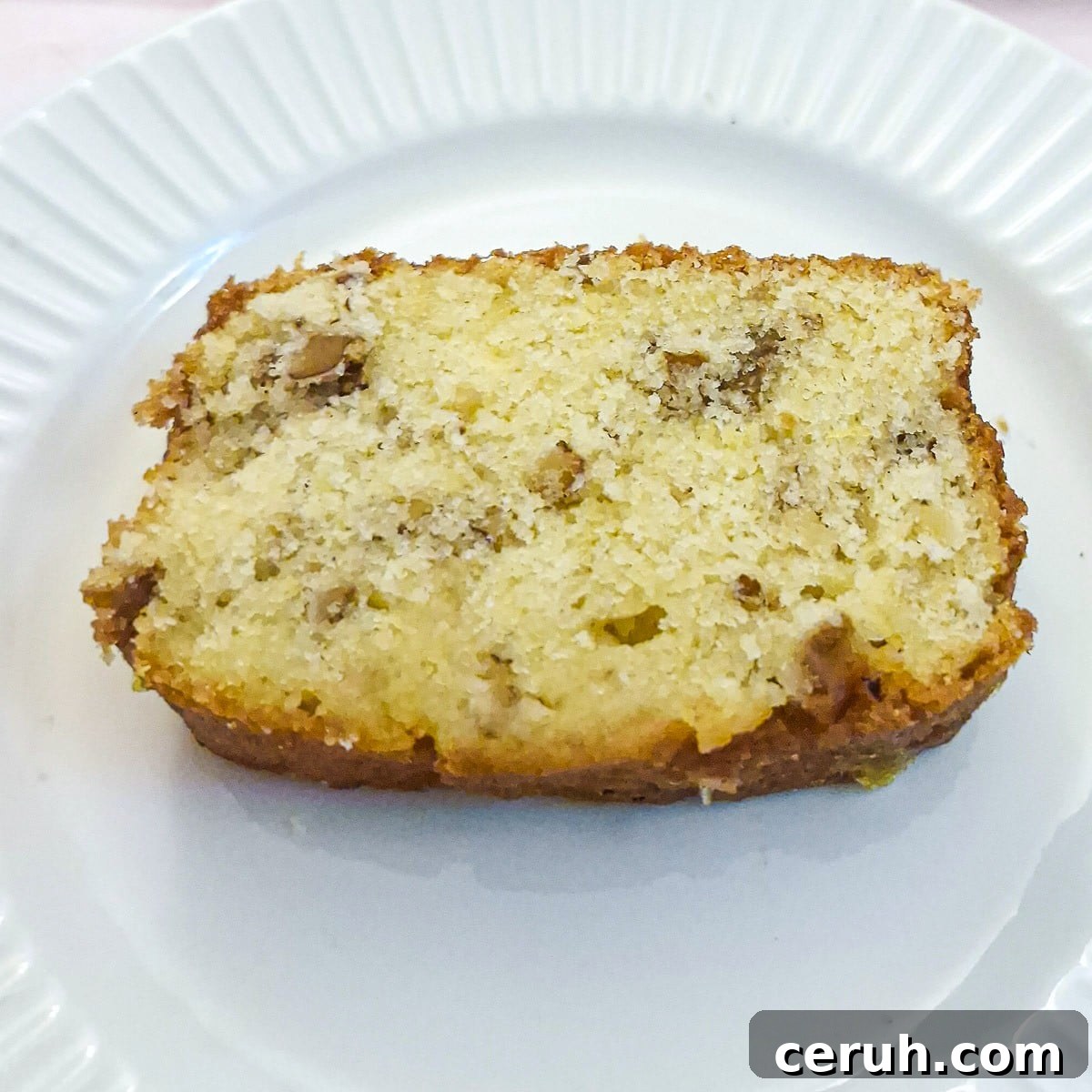 Orange Walnut Drizzle Cake with Zesty Citrus Glaze 3 Close up of a slice of orange walnut drizzle cake on a white plate.