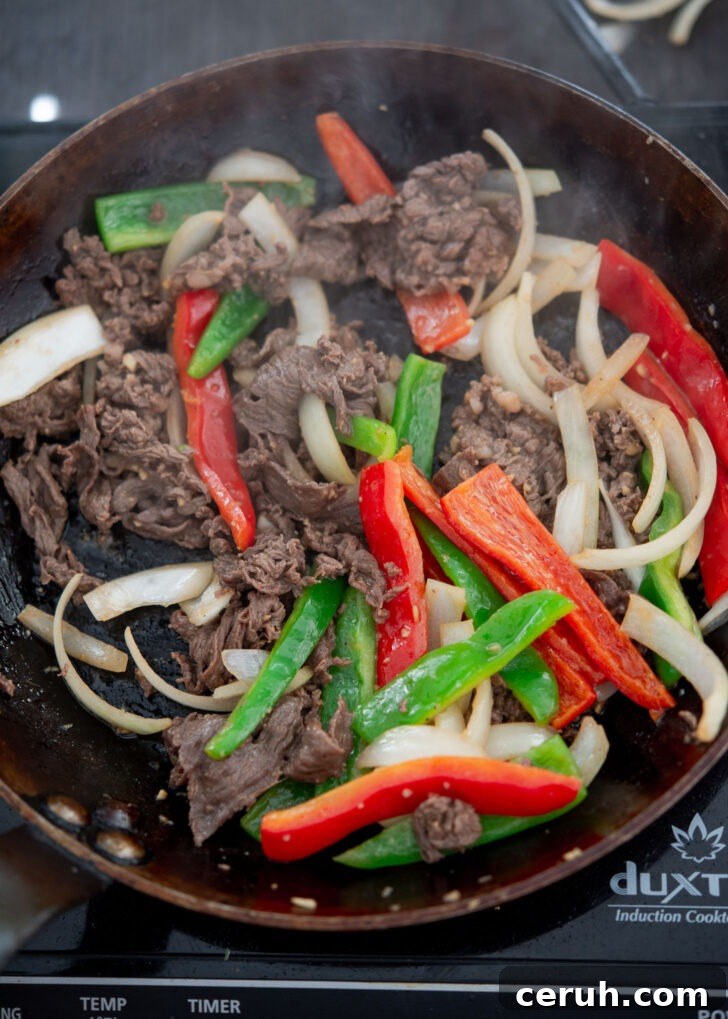 Adding vegetables to the beef in a skillet.