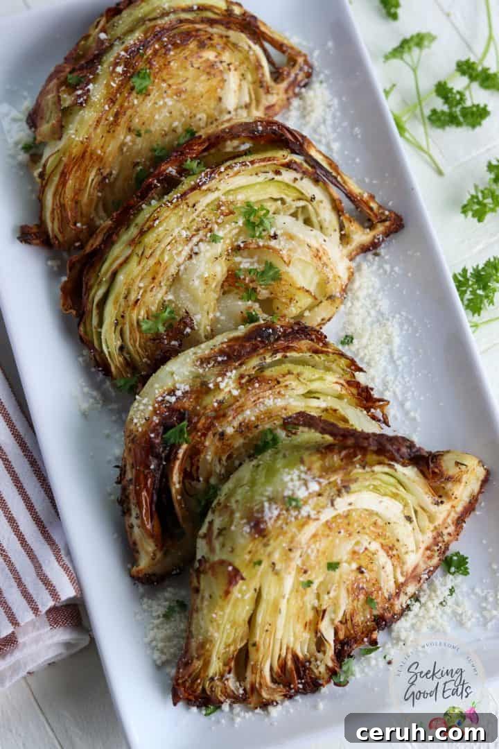 Four cabbage wedges served on a white platter and garnished with parsley and parmesan cheese.