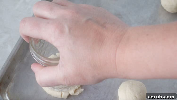 Lemon Sugar Cookies Recipe with Video Tutorial 7 hand pressing glass onto ball of cookie dough to flatten