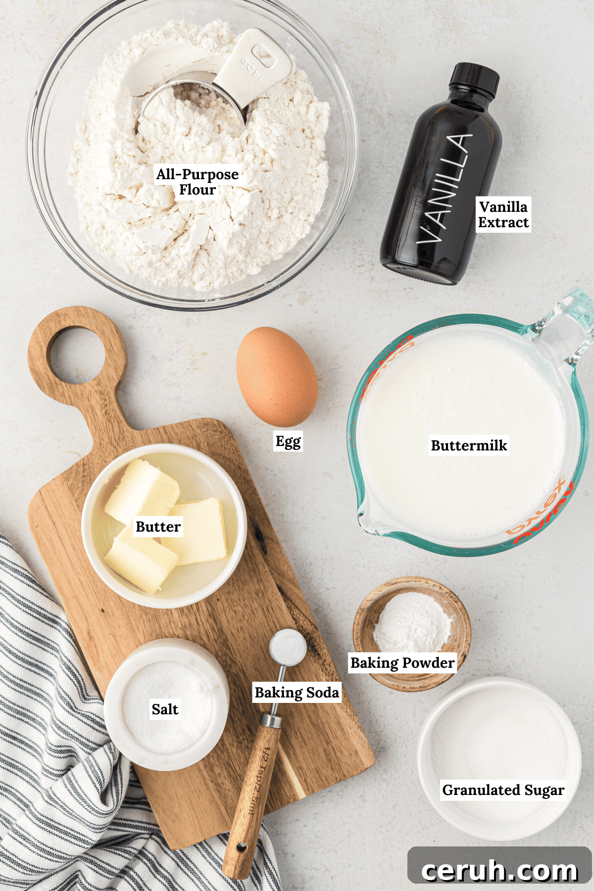 overhead view of the ingredients for buttermilk pancakes including all-purpose flour, vanilla extract, one large egg, buttermilk, baking powder, butter, salt, baking soda and granulated sugar