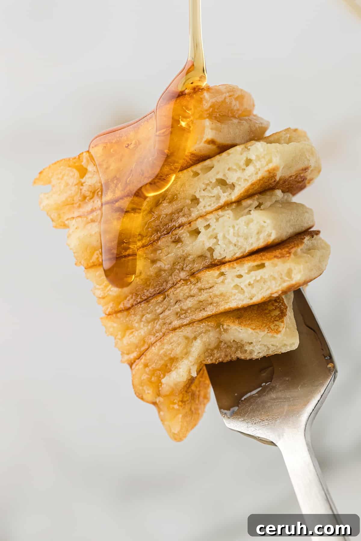 a fork with 5 bite-sized slices of buttermilk pancake on it being drizzles with syrup