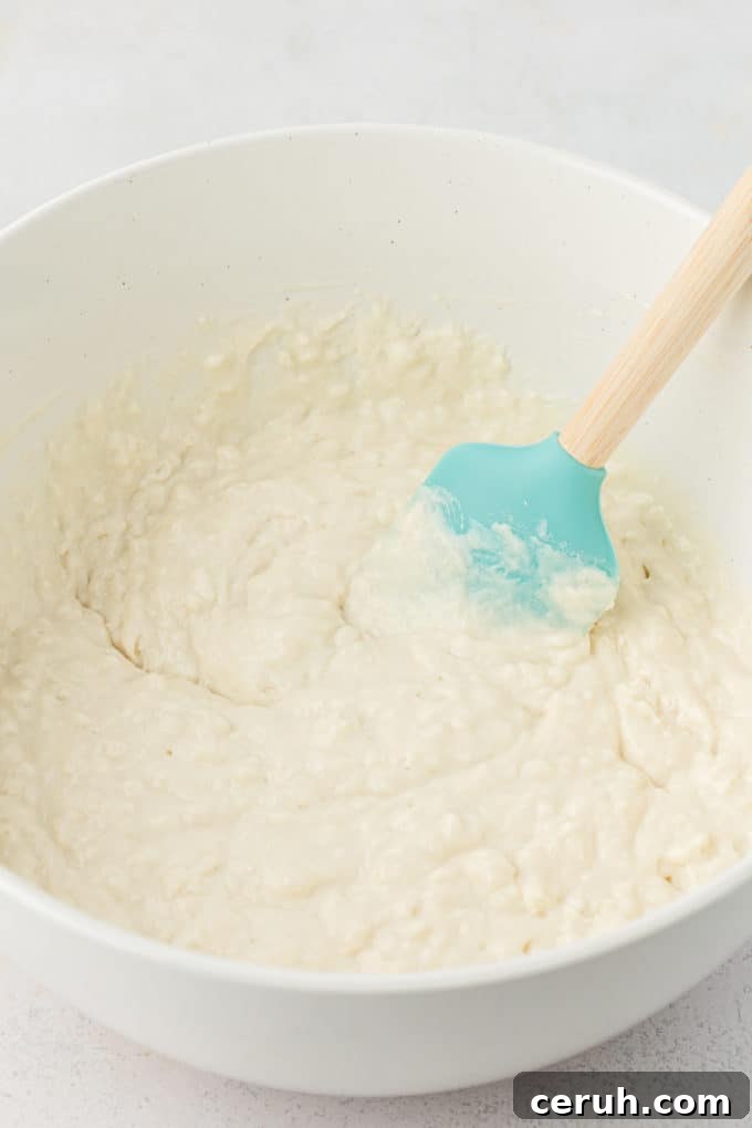 buttermilk pancake batter being stired in a white bowl with a teal spatula