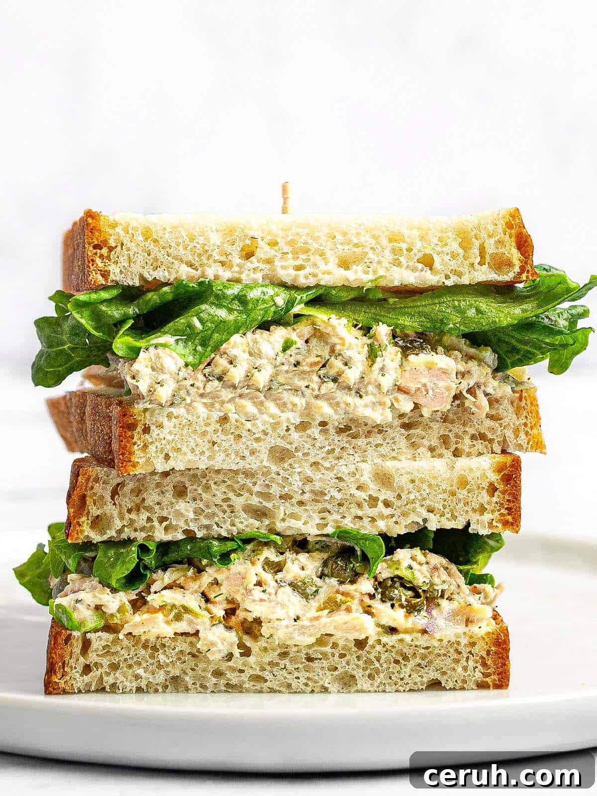 Tuna sandwich with lettuce sliced in half and stacked on a white plate.