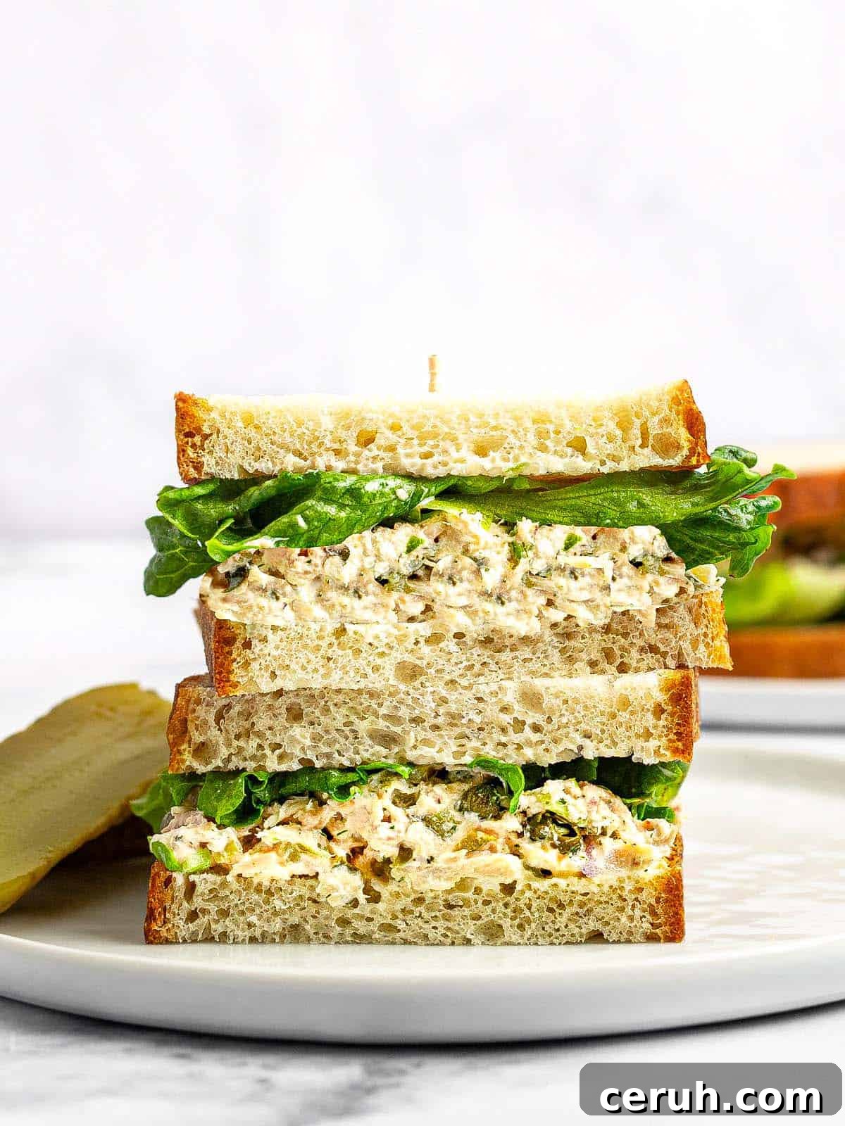 Tuna sandwich with lettuce sliced in half and stacked on a white plate.