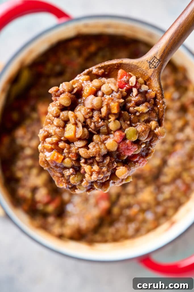 Close-up of a wooden spoon lifting a portion of cooked lentil Bolognese.