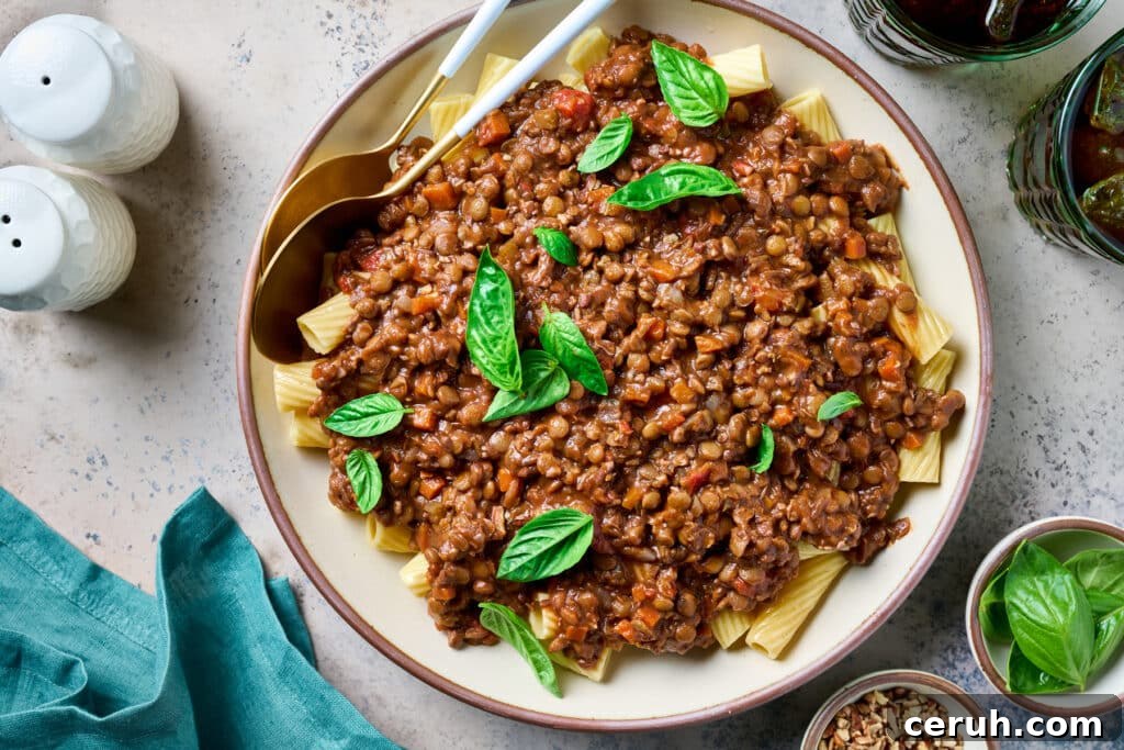 A bowl of rigatoni pasta topped with lentil Bolognese sauce, garnished with fresh basil leaves