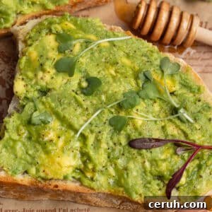 This is a square picture of a close up avocado toast with honey.