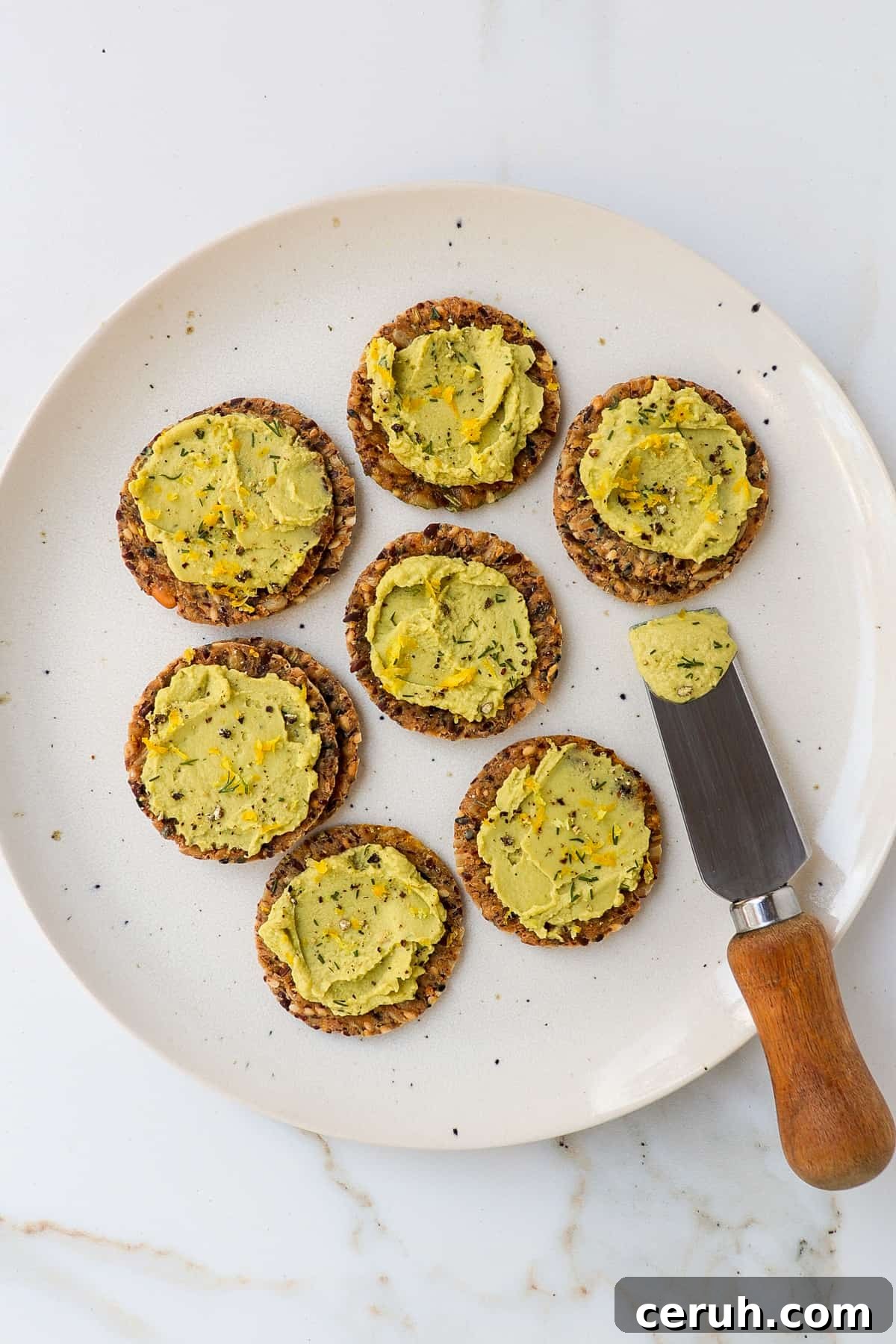 Crackers on a plate spread with dill hummus.