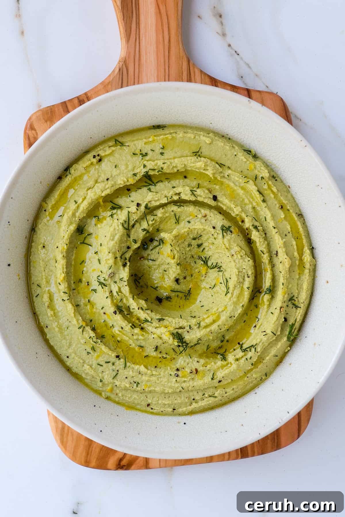 Lemon dill hummus in a bowl on wooden board.