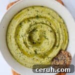 Lemon dill hummus in a bowl with cracker on wooden board.