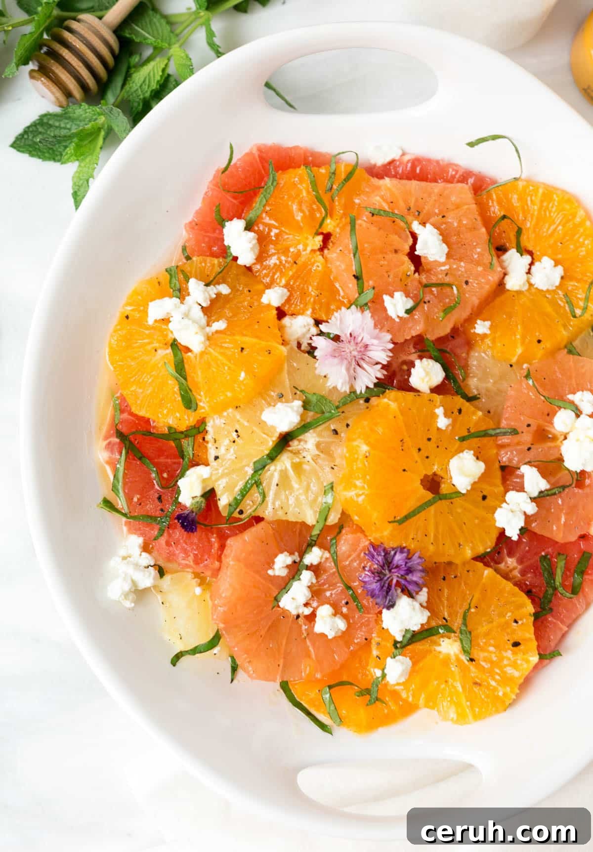 citrus salad with crumbled goat cheese, herbs, and edible flowers in a white serving dish