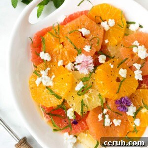 citrus salad with crumbled goat cheese, herbs, and edible flowers in a white serving dish