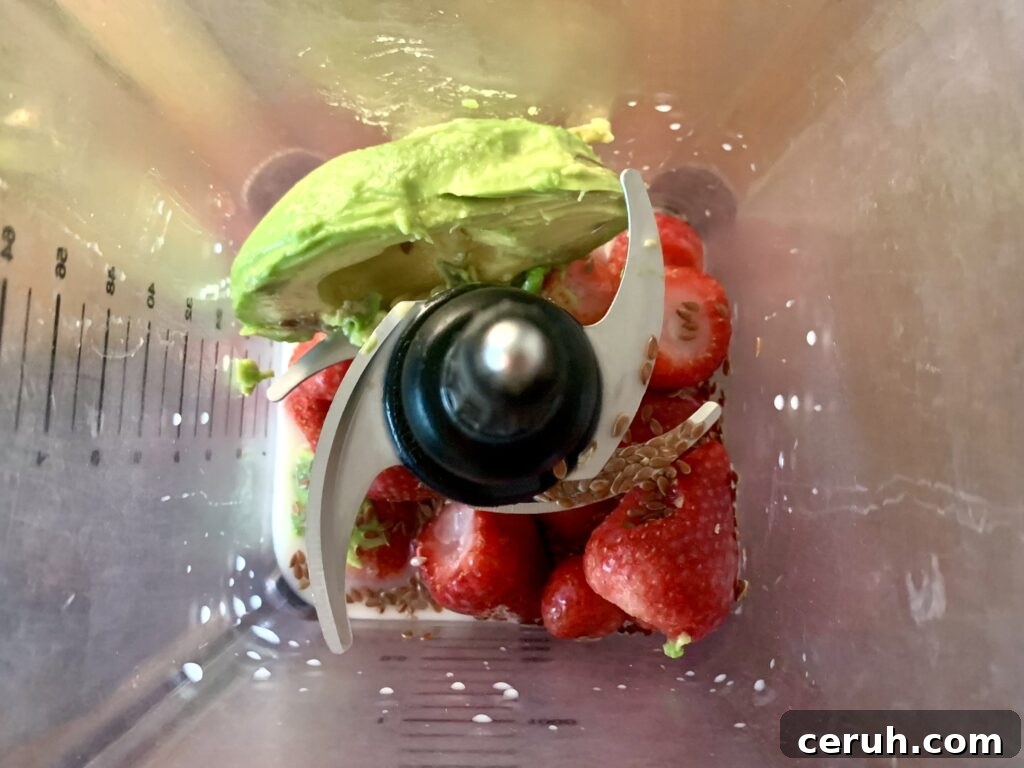 Top down view of a blender with avocado, flax seed, strawberries, and almond milk.
