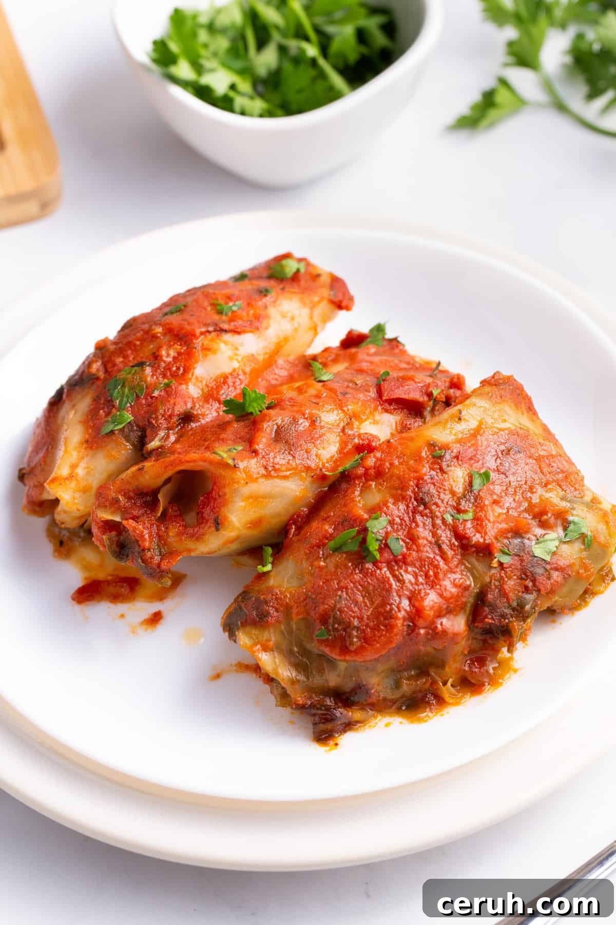 three crockpot cabbage rolls served on a white round plate.