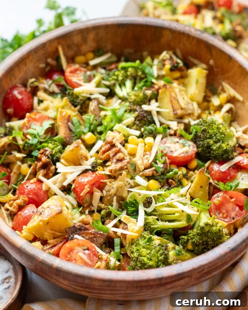 overhead view of a vegan potato salad with yukon gold potatoes, roasted broccoli, corn, cherry tomatoes, bacon walnuts, and dairy free smoked gouda cheese.