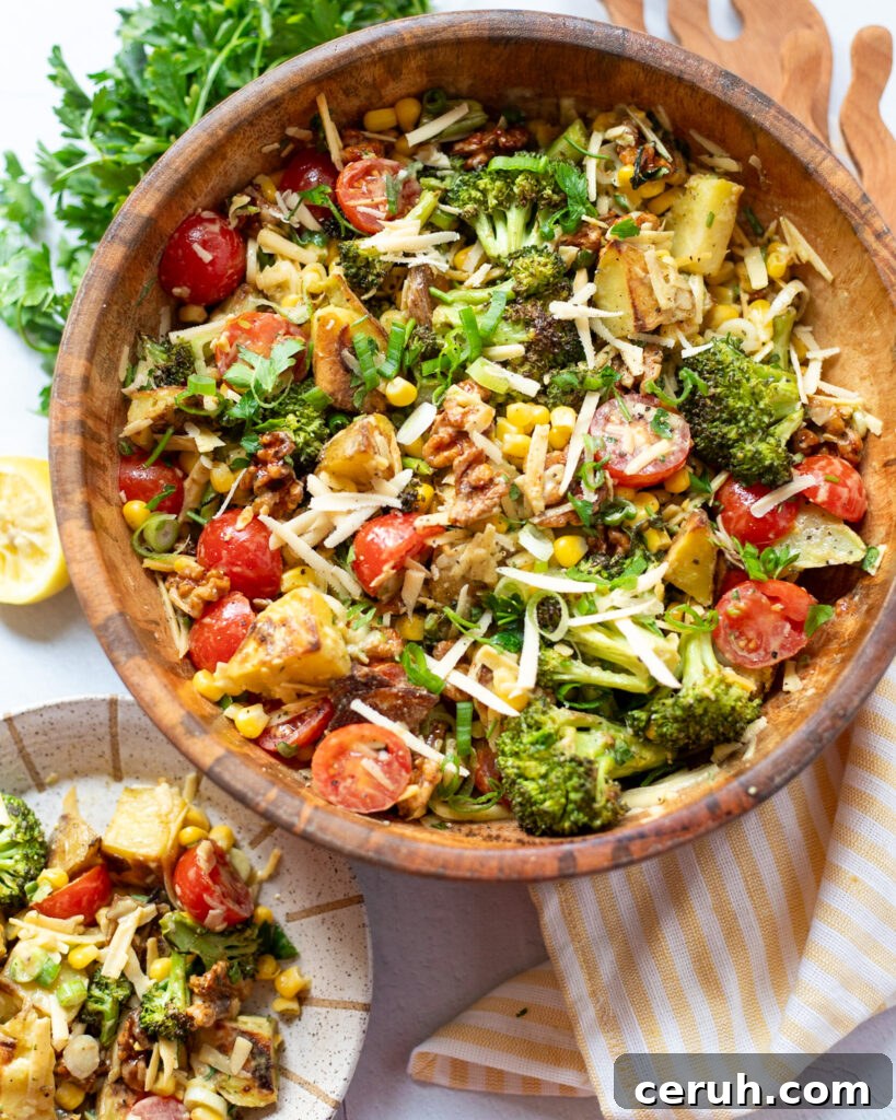 serving dairy free potato salad with cherry tomatoes, bacon walnuts, roasted broccoli, frozen corn and more from a wooden serving bowl to a ceramic plate.