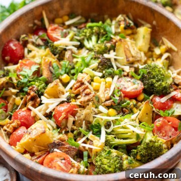 overhead view of a wooden serving bowl with a vegan potato salad made with crispy roasted potatoes, broccoli, cherry tomatoes, and smoked gouda in a lemony maple dijon vinaigrette.
