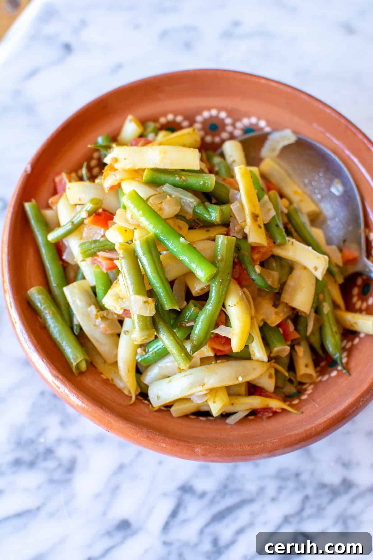 A terracotta dish filled with green beans and yellow wax beans and tomatoes all cooked together.