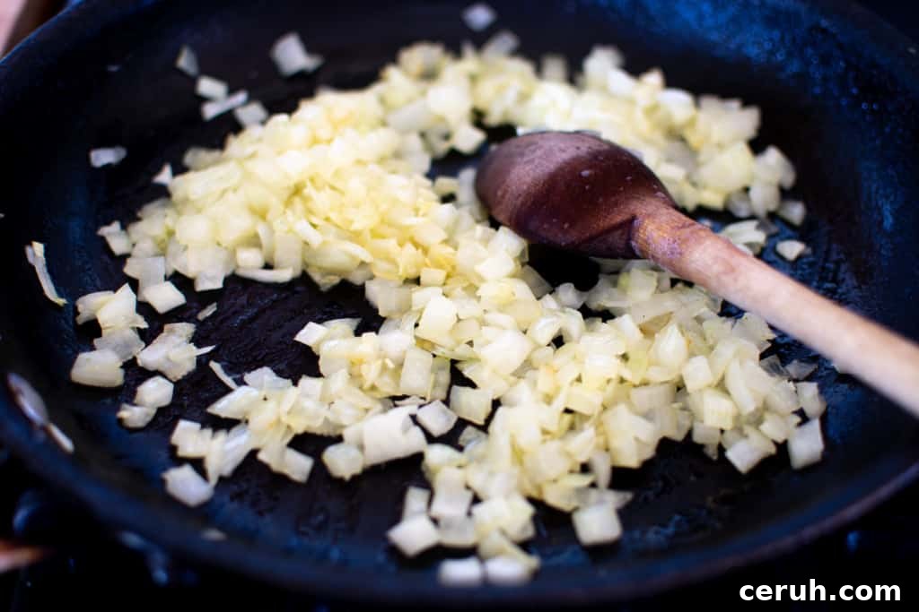 Chopped onions in a black frying pan with a wood spoon in the pan. The onions are a little golden and sautéed but not brown.