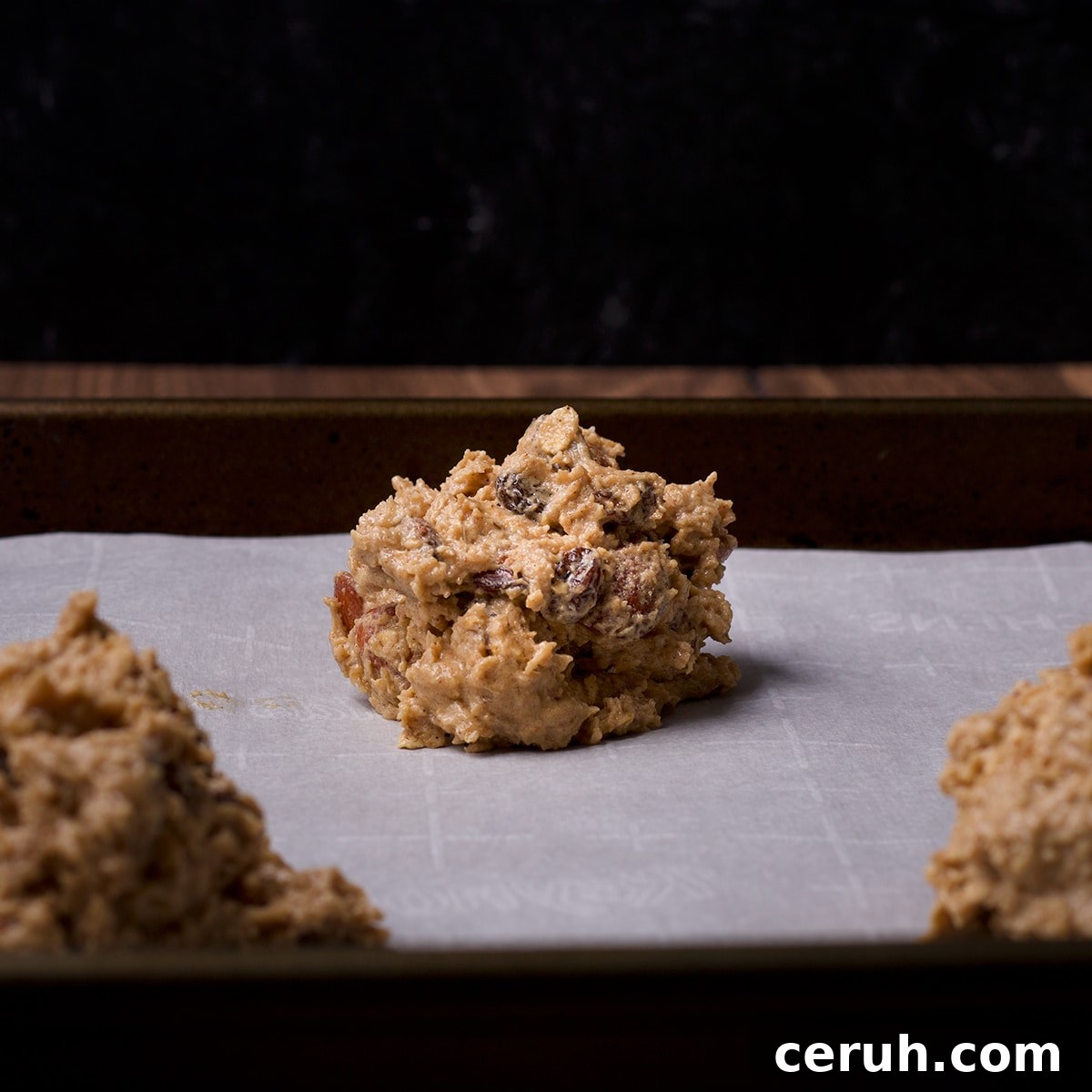 Balls of oatmeal raisin cookie dough on a parchment lined baking sheet, ready to bake.