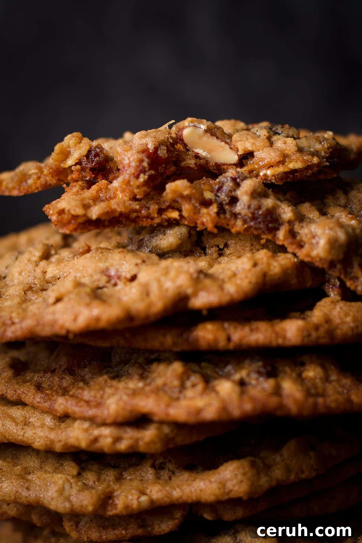 A stack of oatmeal raisin cookies with the top cookie broken in half to reveal the soft, chewy center.