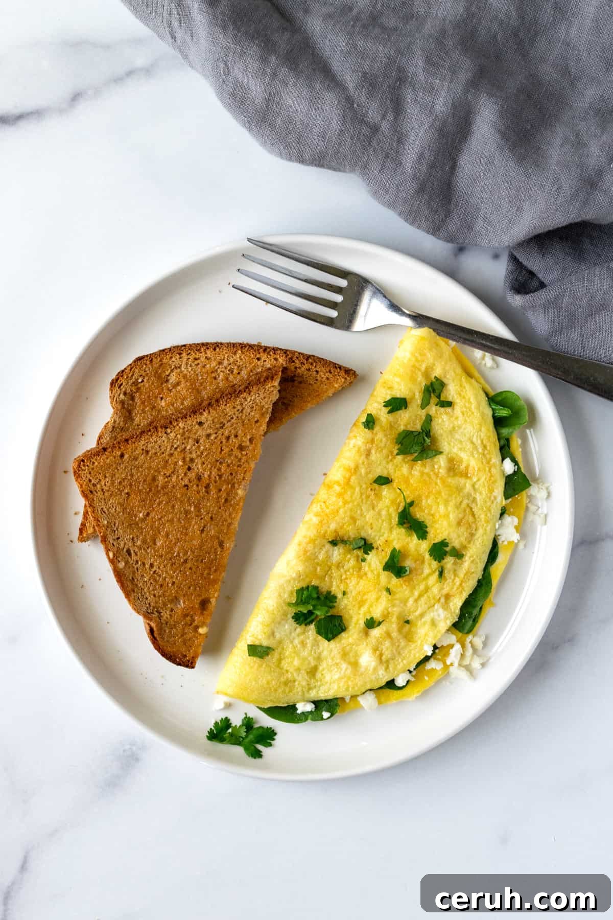 Omelette with Spinach and Feta on a white plate with toast with a fork.