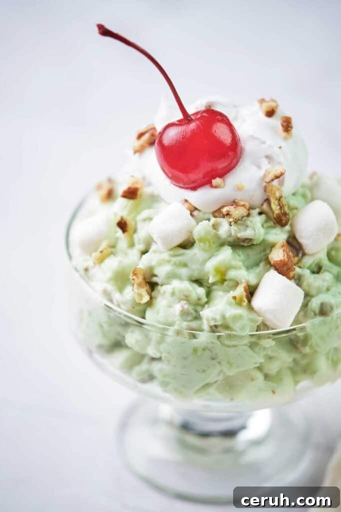 pistachio fluff salad in a glass dish topped with a maraschino cherry