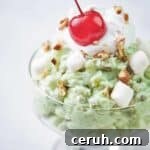 close up of pistachio fluff in glass dish topped with a cherry