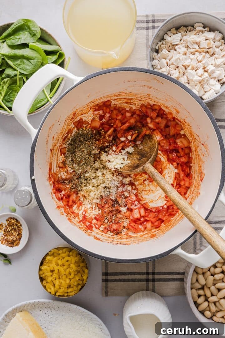 Onions, tomato paste, and spices being sauteed in a white Dutch oven.
