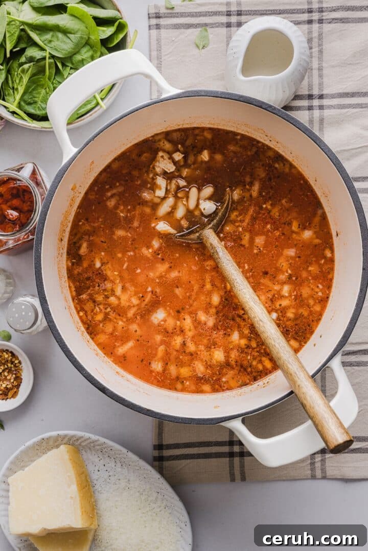 Beans stirred into marry me chicken soup in a large white pot.