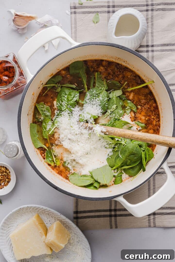 Spinach, cream, and grated parmesan being added to marry me chicken soup in a large white pot.