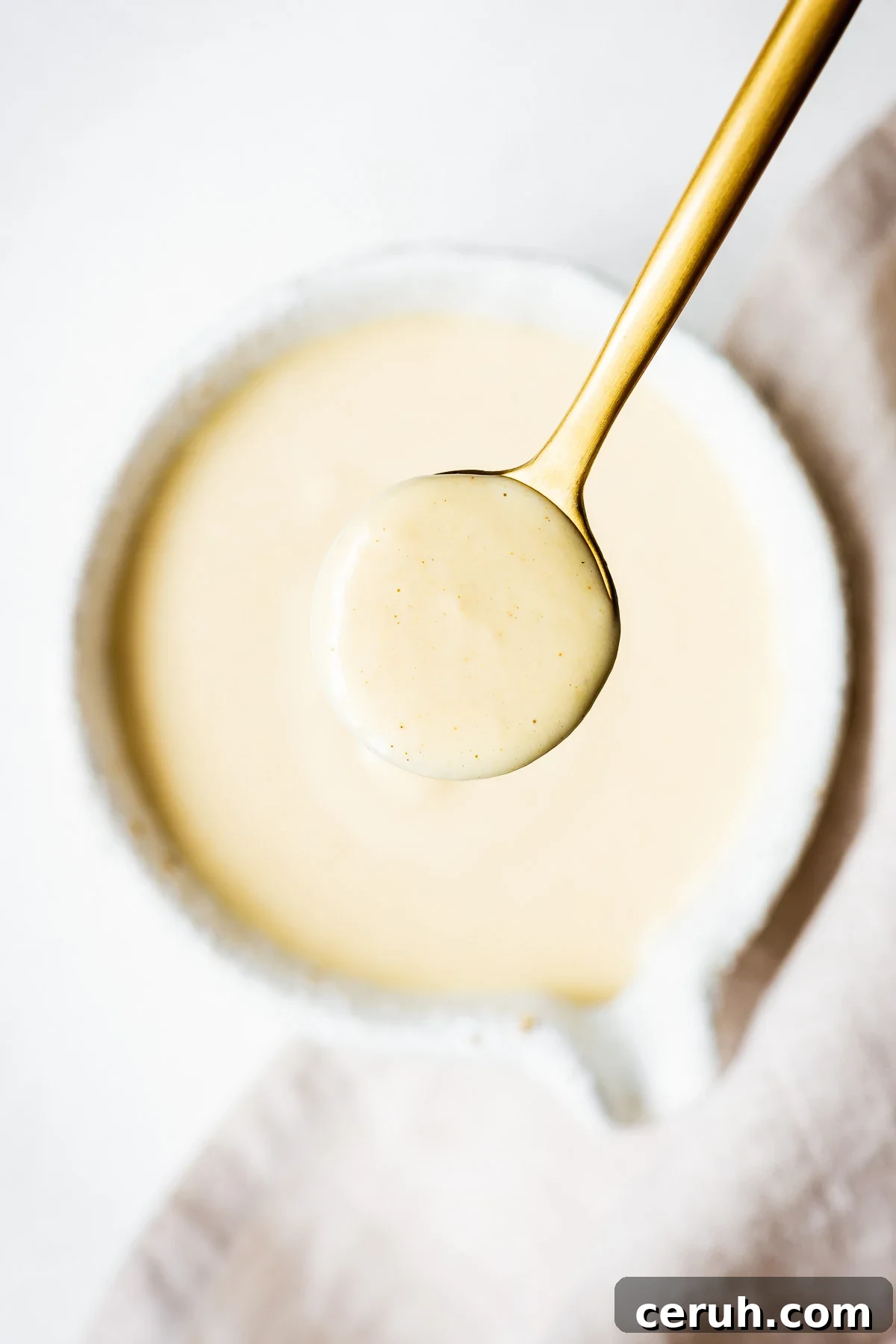 Creamy maple tahini dressing in a golden spoon viewed from above.