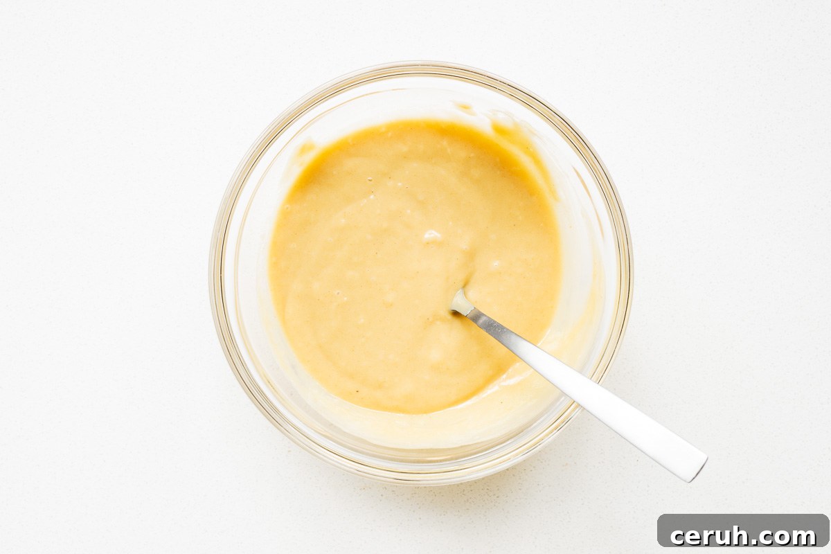 Thick tahini mixture for tahini dressing in a glass bowl viewed from above.