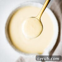 Creamy maple tahini dressing in a golden spoon viewed from above.