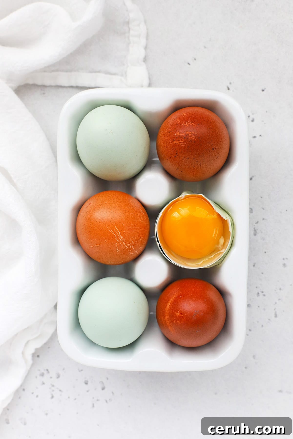 Overhead view of an egg carton with 6 eggs. One egg is open, revealing a golden yolk