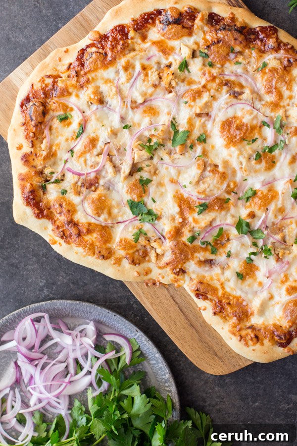 Barbeque Chicken Pizza on a cutting board, sitting next to a plate of flat leaf parsley and sliced red onions.