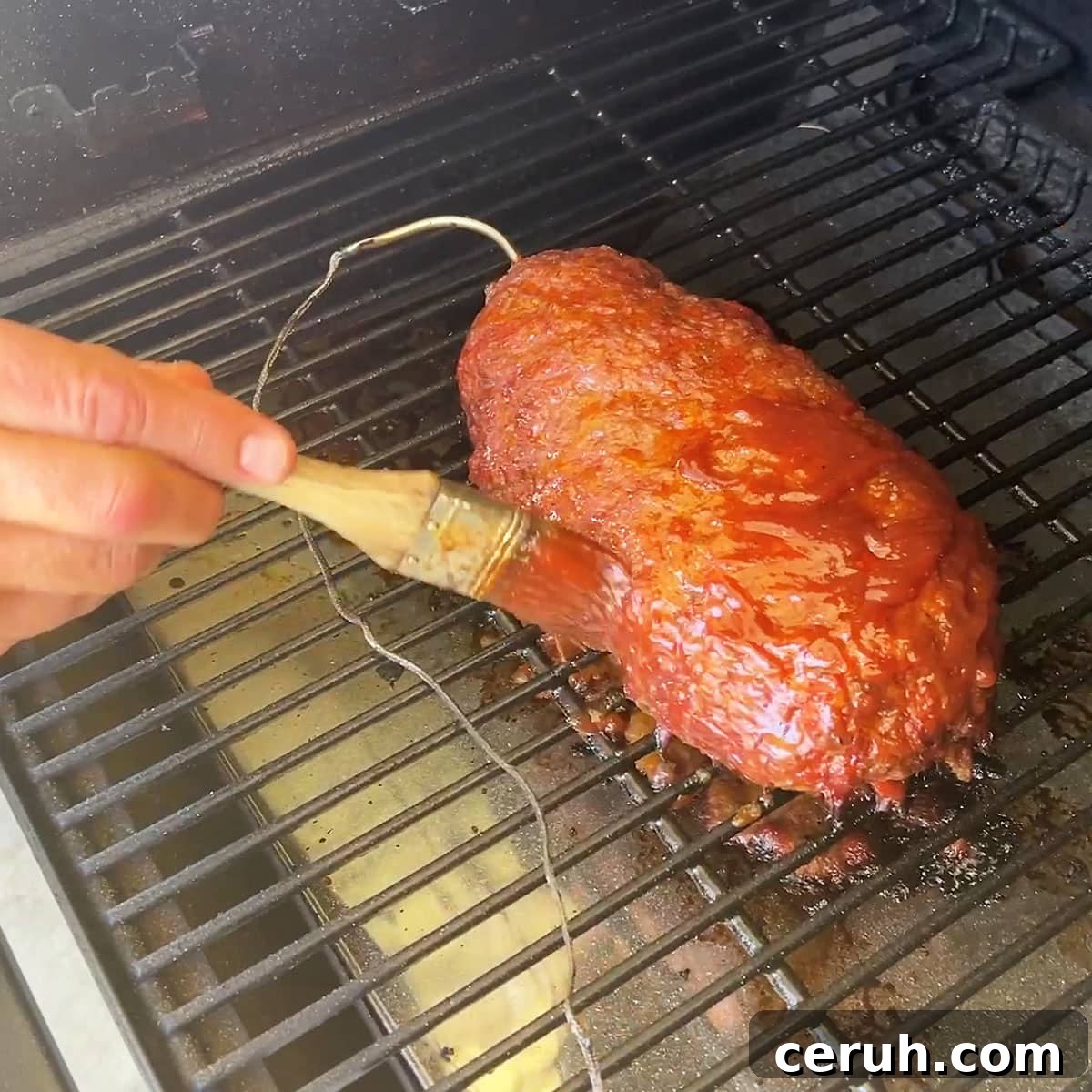 Brushing barbecue sauce and ketchup on the outside as the meatloaf cooks.